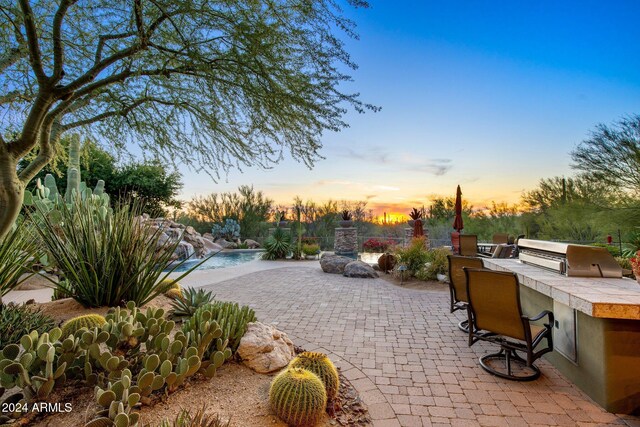 patio terrace at dusk featuring pool water feature, a grill, and exterior kitchen