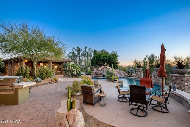 patio terrace at dusk featuring area for grilling and pool water feature