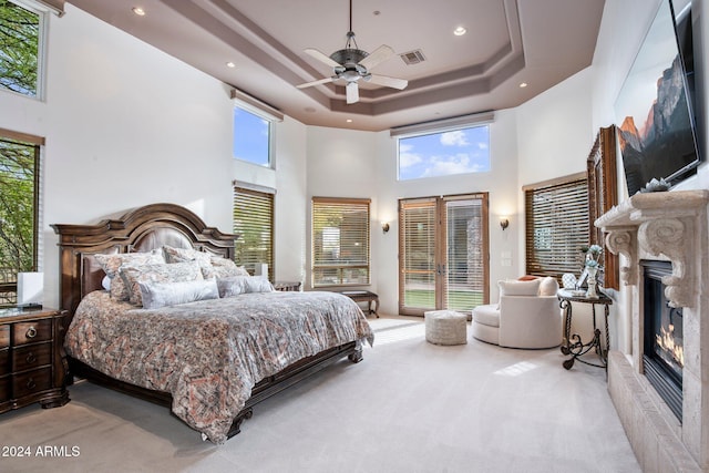 bedroom featuring light carpet, french doors, a raised ceiling, ceiling fan, and a high ceiling