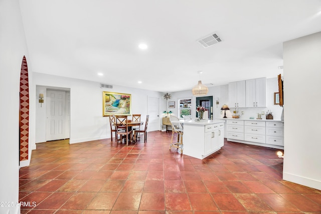 kitchen featuring hanging light fixtures, a center island, white cabinets, and a kitchen bar