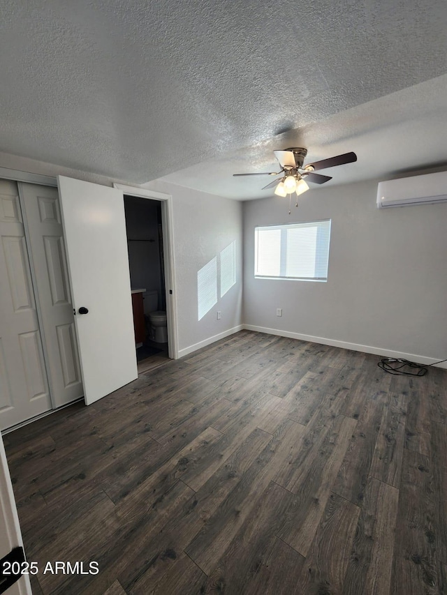 empty room featuring a textured ceiling, dark wood-type flooring, a wall unit AC, and ceiling fan