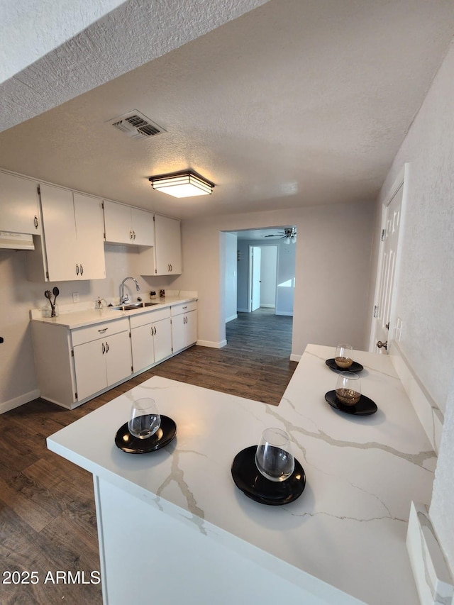 kitchen with kitchen peninsula, a textured ceiling, dark hardwood / wood-style floors, white cabinetry, and sink