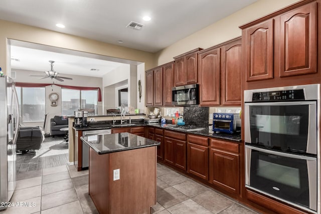 kitchen featuring sink, backsplash, dark stone counters, light tile patterned flooring, and appliances with stainless steel finishes