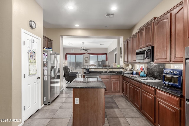 kitchen featuring dark stone counters, stainless steel appliances, sink, a center island, and light tile patterned flooring