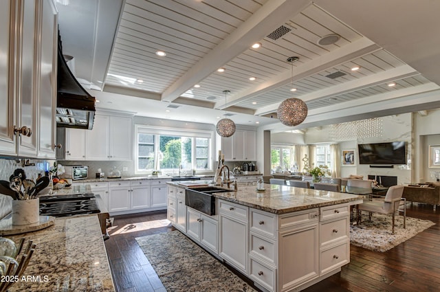 kitchen with white cabinetry, sink, hanging light fixtures, light stone countertops, and a center island with sink