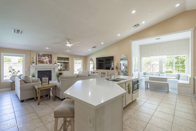 kitchen with lofted ceiling, an island with sink, sink, light tile patterned floors, and ceiling fan