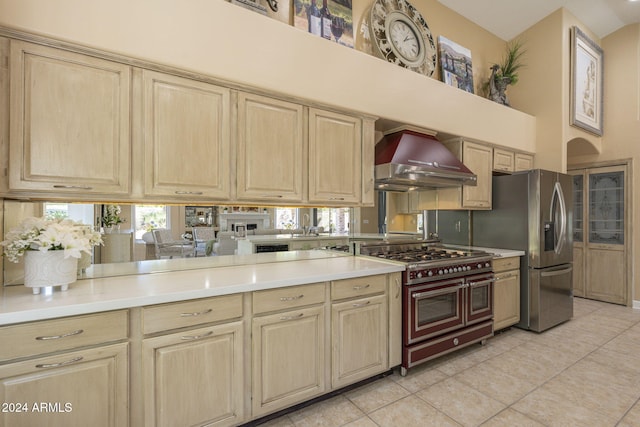 kitchen with light brown cabinets, wall chimney range hood, kitchen peninsula, stainless steel appliances, and light tile patterned floors