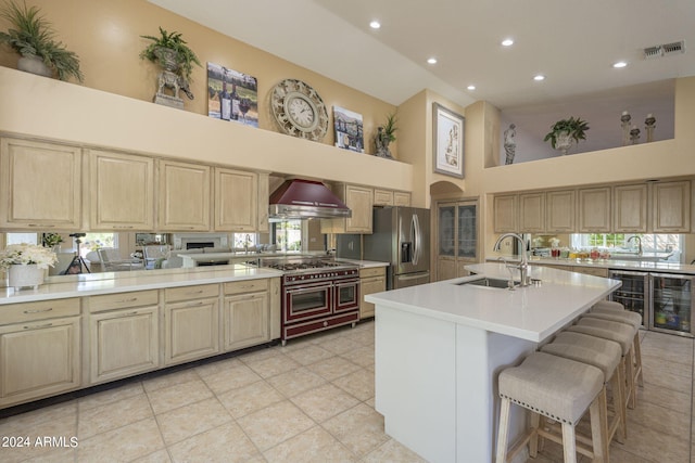 kitchen with a towering ceiling, sink, a kitchen breakfast bar, stainless steel appliances, and wall chimney exhaust hood