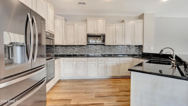 kitchen featuring sink, light hardwood / wood-style flooring, dark stone countertops, appliances with stainless steel finishes, and decorative backsplash