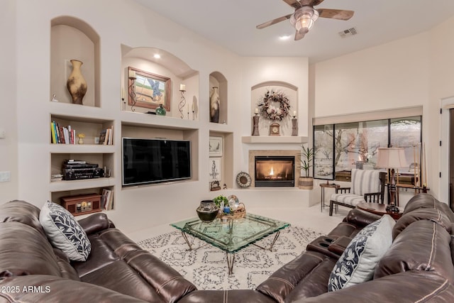 living room featuring built in shelves, a tile fireplace, and ceiling fan