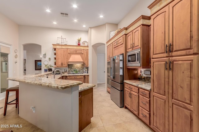 kitchen with light tile patterned floors, a kitchen breakfast bar, backsplash, stainless steel appliances, and light stone counters