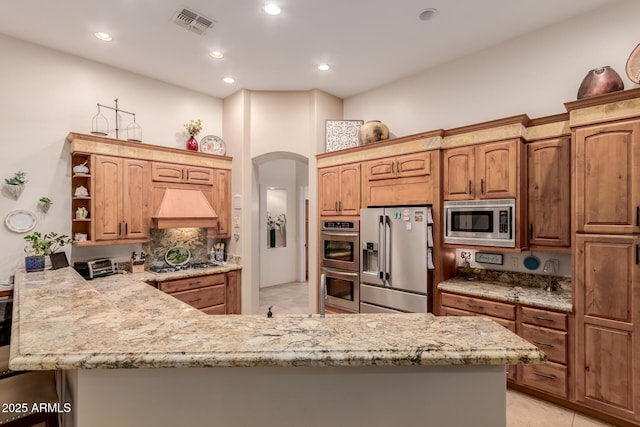 kitchen featuring light stone counters, premium range hood, appliances with stainless steel finishes, and kitchen peninsula