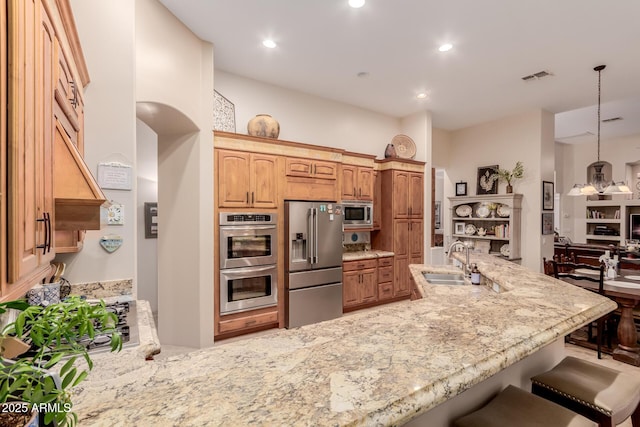 kitchen with appliances with stainless steel finishes, sink, decorative light fixtures, kitchen peninsula, and a breakfast bar