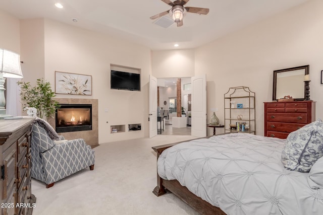 bedroom featuring ceiling fan, a tile fireplace, and light carpet