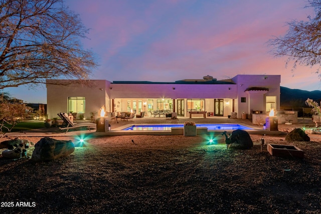 back house at dusk featuring a patio and exterior kitchen