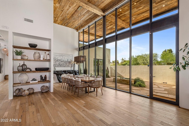 dining room with visible vents, wood-type flooring, wooden ceiling, a wall of windows, and a towering ceiling