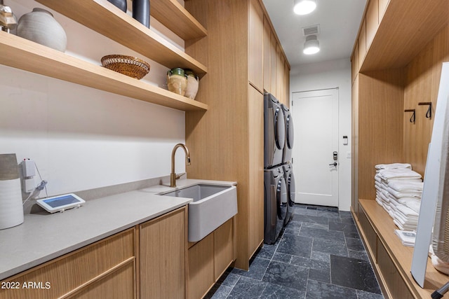 kitchen featuring open shelves, light countertops, stone tile floors, stacked washer / drying machine, and a sink