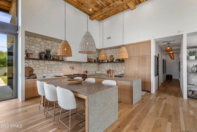 kitchen with light wood finished floors, beamed ceiling, a center island, and open shelves