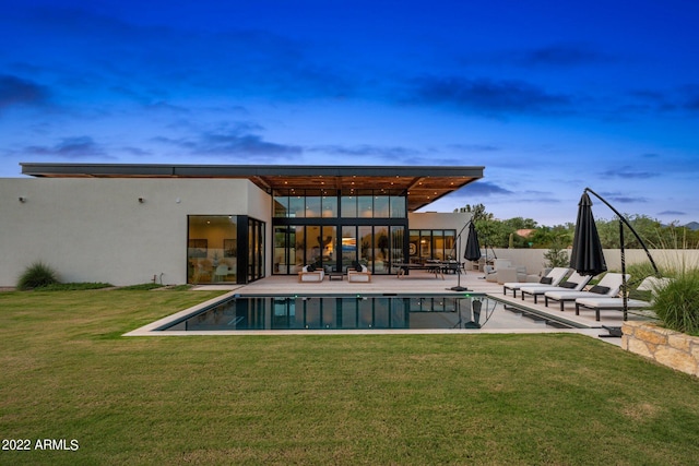 back of house at dusk featuring a yard, a patio, a fenced in pool, and stucco siding