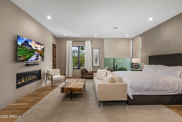 bedroom featuring a glass covered fireplace, recessed lighting, wood finished floors, and visible vents