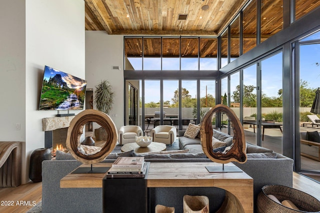 living room with wood finished floors, wood ceiling, a towering ceiling, and a lit fireplace