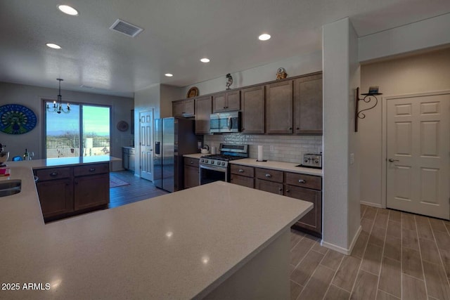 kitchen with stainless steel appliances, visible vents, light countertops, backsplash, and light wood finished floors