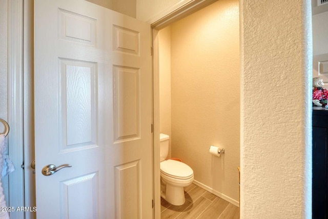 bathroom featuring toilet, a textured wall, baseboards, and wood finish floors