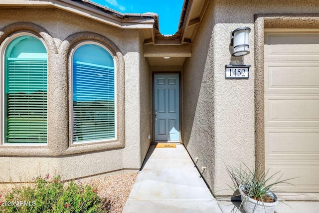 view of exterior entry featuring a garage, a tiled roof, and stucco siding