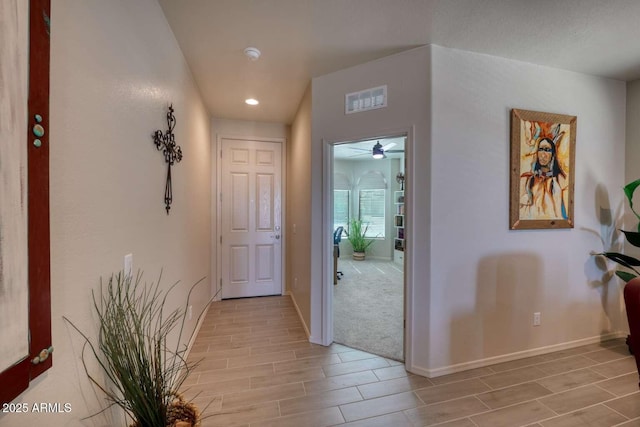 corridor featuring wood tiled floor, visible vents, and baseboards