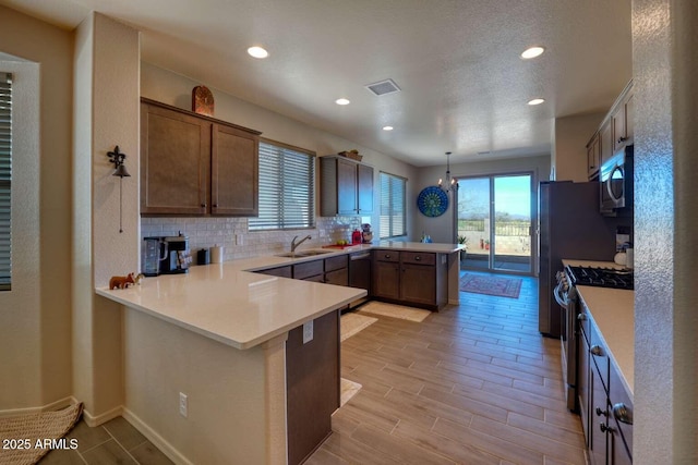 kitchen featuring a peninsula, a sink, light countertops, appliances with stainless steel finishes, and decorative backsplash