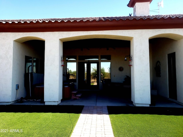 view of exterior entry featuring stucco siding, a tiled roof, and a lawn