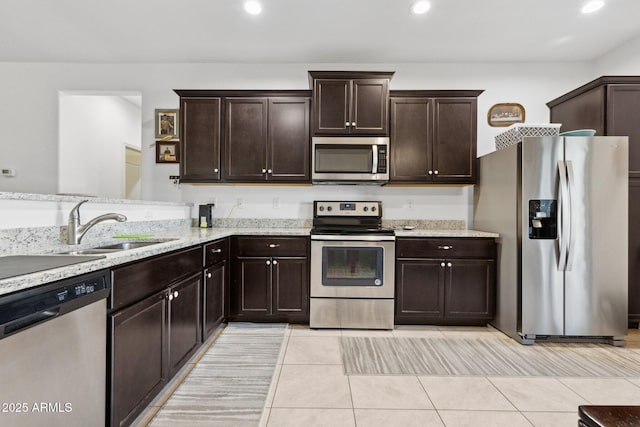 kitchen with light tile patterned flooring, dark brown cabinetry, sink, appliances with stainless steel finishes, and light stone countertops