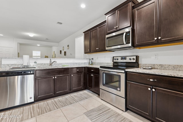 kitchen featuring sink, light tile patterned floors, dark brown cabinets, stainless steel appliances, and light stone countertops