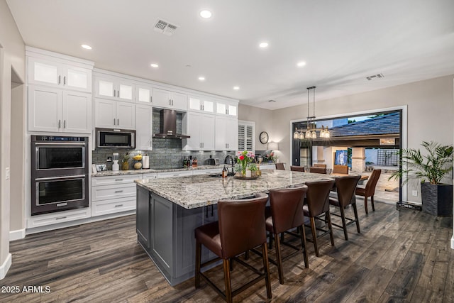 20866 W Werner Pl, Buckeye, AZ 85396 - kitchen featuring black appliances, wall chimney exhaust hood, dark wood-style flooring, a kitchen island with sink, and recessed lighting