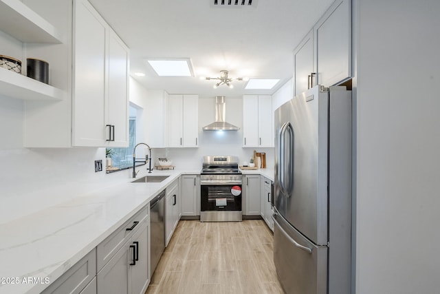 kitchen with a sink, wall chimney range hood, appliances with stainless steel finishes, white cabinetry, and open shelves