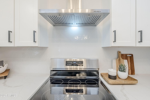 kitchen with electric range, white cabinetry, light stone countertops, and wall chimney range hood