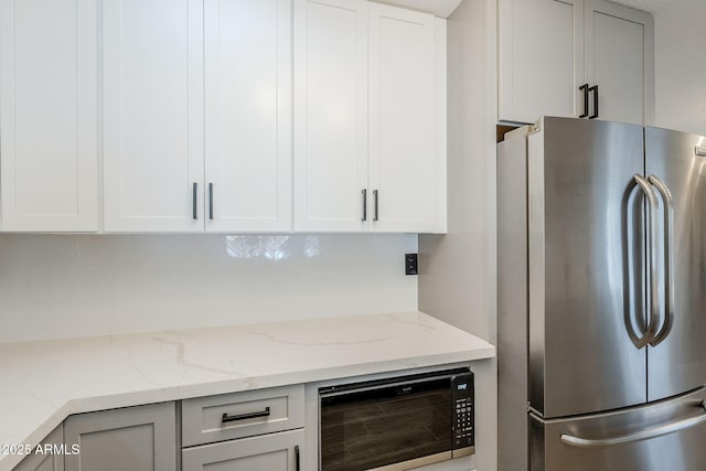 kitchen featuring light stone countertops, white cabinetry, black microwave, and freestanding refrigerator