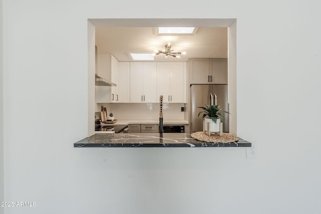 kitchen with under cabinet range hood, a peninsula, a skylight, freestanding refrigerator, and electric stove