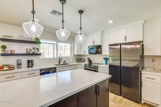 kitchen featuring appliances with stainless steel finishes, sink, backsplash, white cabinetry, and hanging light fixtures