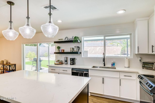 kitchen with stove, hanging light fixtures, backsplash, stainless steel dishwasher, and sink