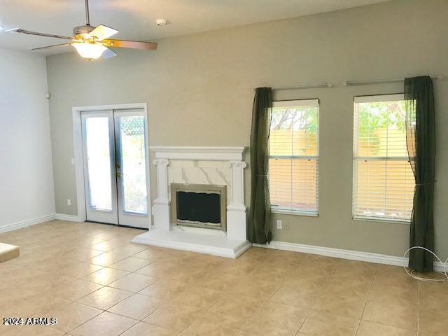 unfurnished living room featuring ceiling fan, french doors, a high end fireplace, and light tile patterned floors