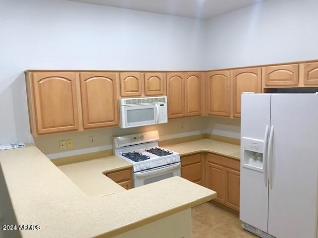 kitchen with a towering ceiling, light brown cabinetry, white appliances, and light tile patterned floors