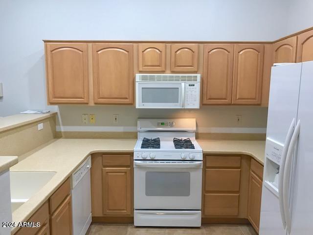 kitchen featuring light tile patterned flooring, white appliances, and light brown cabinetry