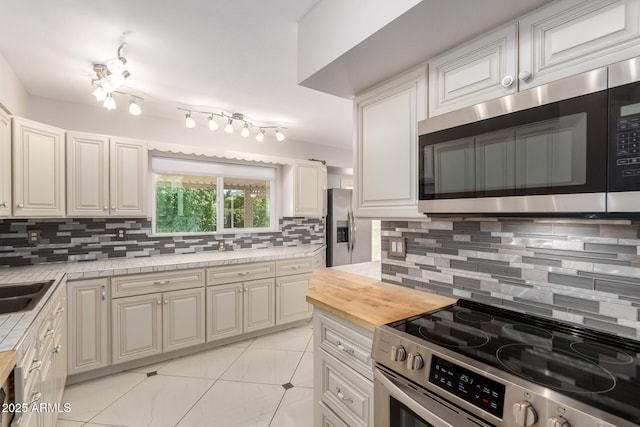 9603 W Calico Dr, Sun City, AZ 85373 - kitchen featuring stainless steel appliances, tasteful backsplash, light tile patterned flooring, butcher block counters, and rail lighting