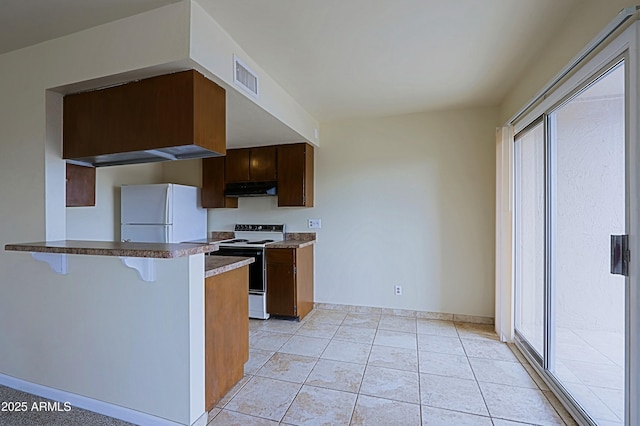 kitchen featuring under cabinet range hood, electric range, visible vents, freestanding refrigerator, and a kitchen bar