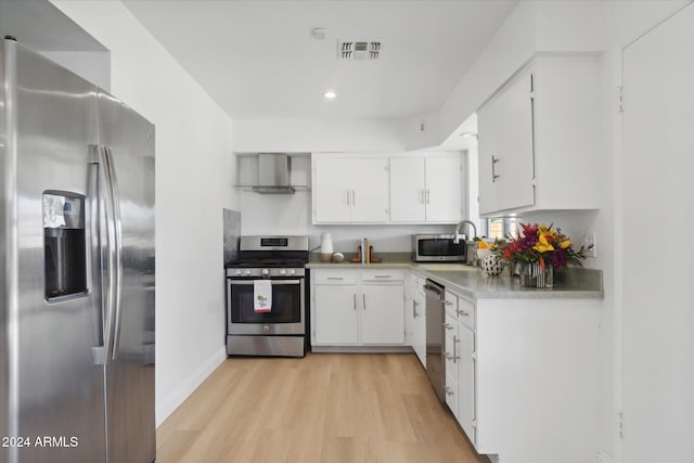 kitchen featuring wall chimney range hood, sink, light wood-type flooring, stainless steel appliances, and white cabinets