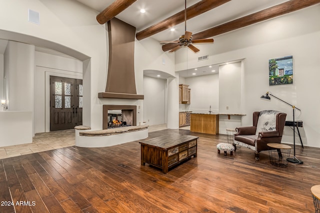 living room with a towering ceiling, wood-type flooring, a fireplace, ceiling fan, and beamed ceiling