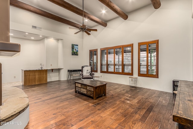 living room with a towering ceiling, beamed ceiling, dark wood-type flooring, and ceiling fan