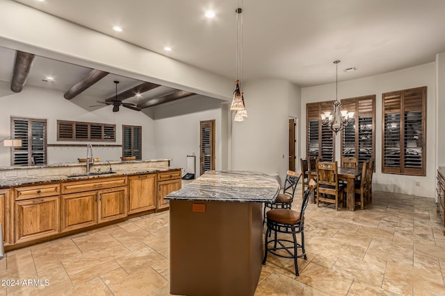 kitchen featuring a breakfast bar, beam ceiling, a sink, dark stone counters, and stone tile flooring