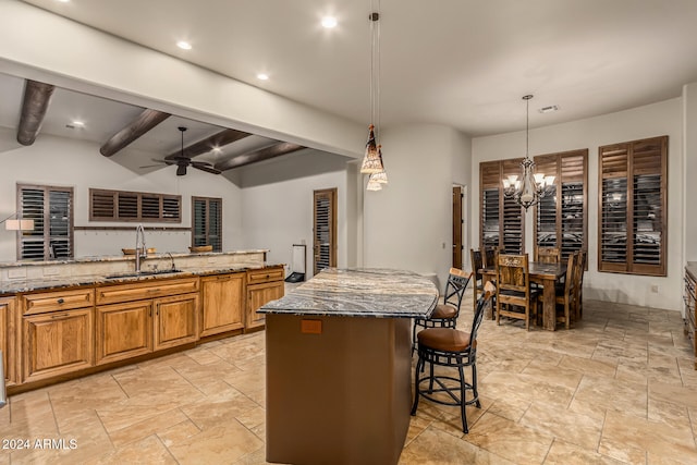 kitchen with stone counters, sink, ceiling fan with notable chandelier, a center island, and pendant lighting